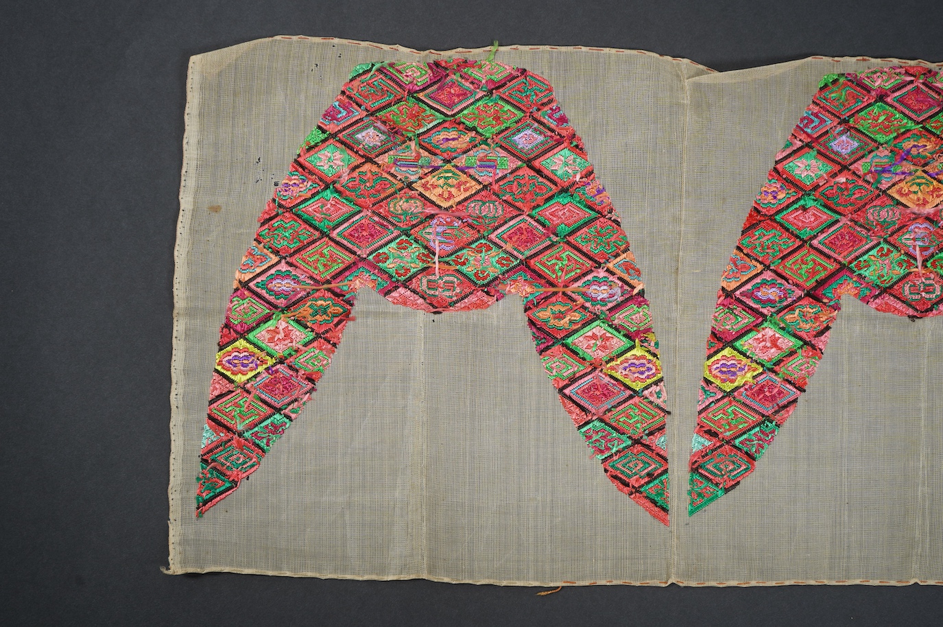 A pair of early 20th century Chinese silk polychrome finely embroidered slipper fronts, possibly from Guangxi province. Embroidered in a diamond grid, with stylistic and symbolic motifs. 21.5cm top to base. Condition - u